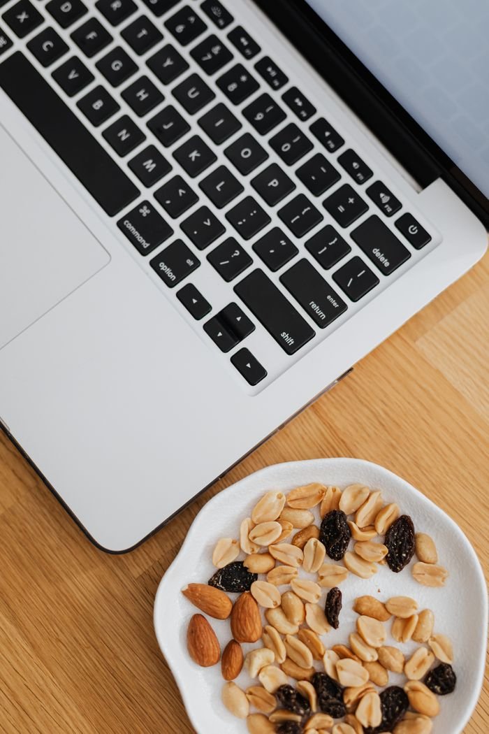 Plate of almonds, peanuts, and raisins beside open laptop. Perfect for work-from-home snack inspiration.