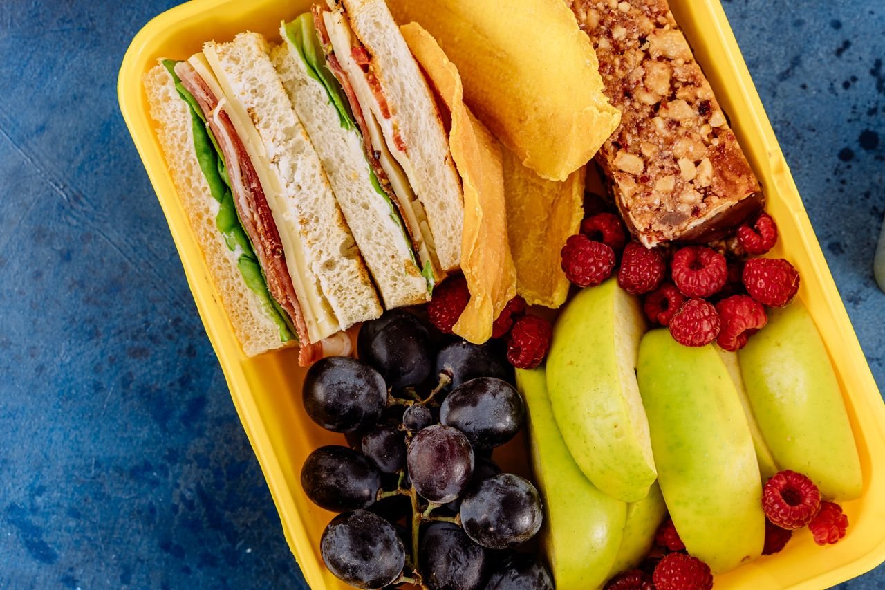 Vibrant lunchbox containing a sandwich, fresh fruits, and a snack bar, ideal for healthy meals.