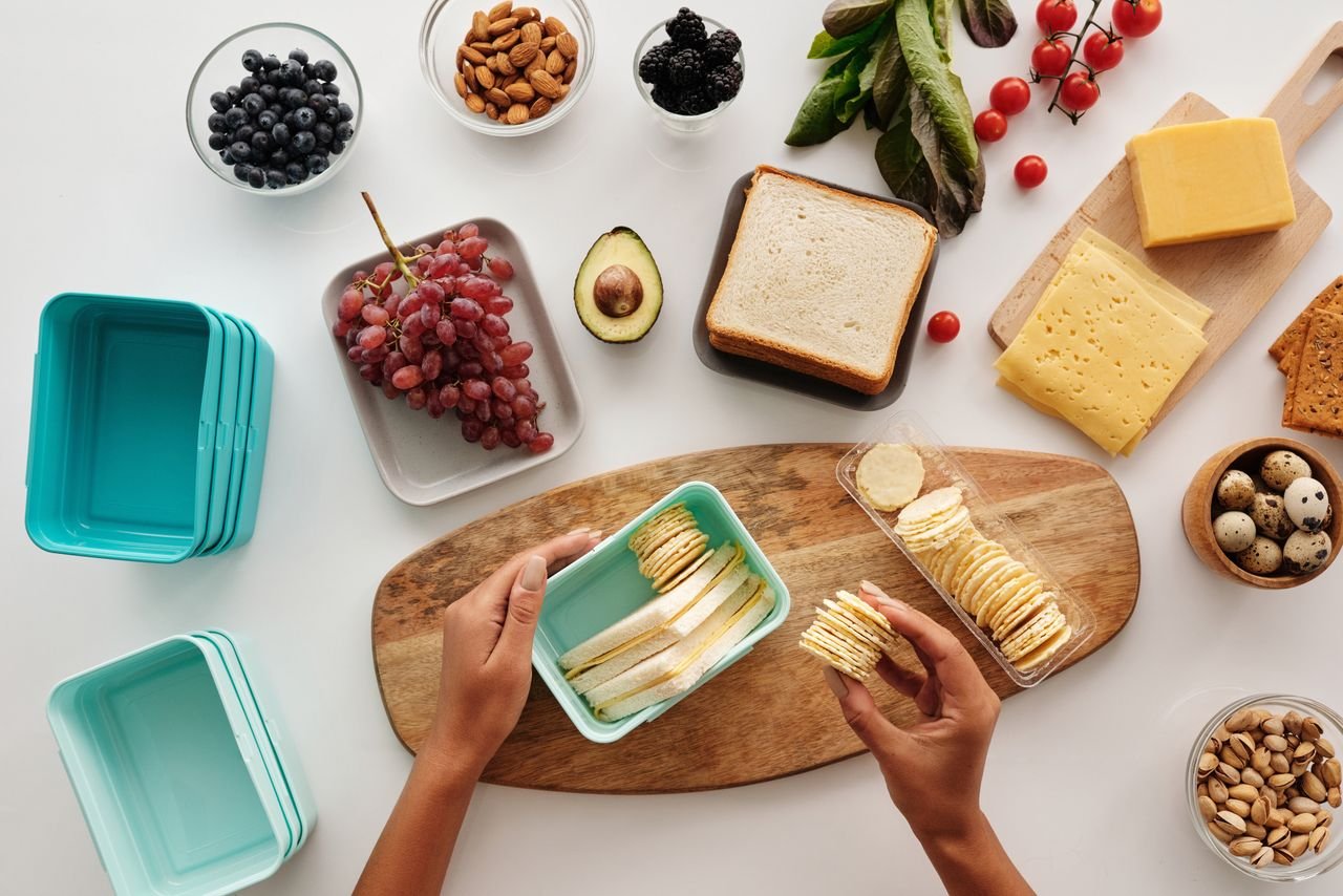 Top view of preparing a healthy lunch with fruits, cheese, and crackers, showcasing fresh ingredients and a vibrant lifestyle.