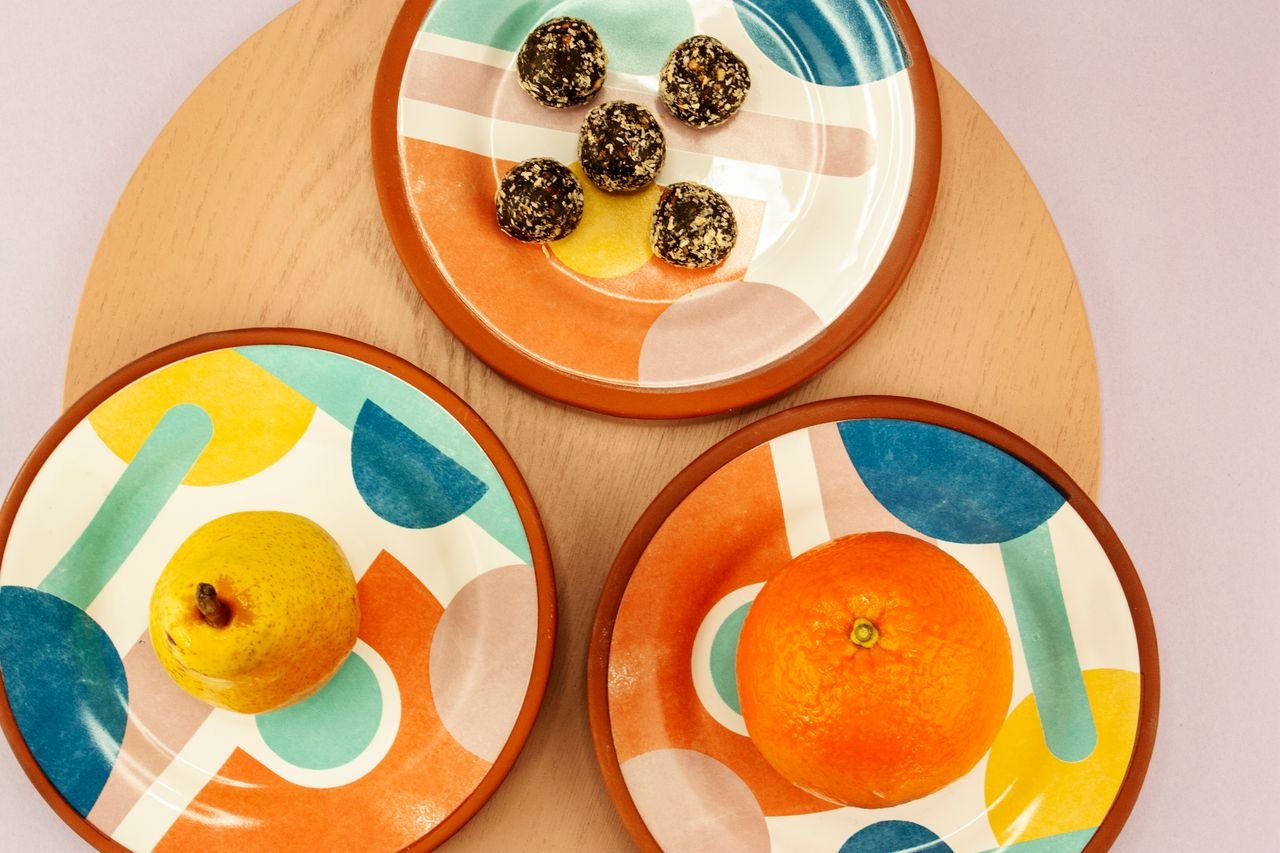 Vibrant geometric plates showcasing a pear, an orange, and snacks on a wooden tray.